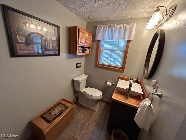 half bath featuring a textured ceiling, vanity, toilet, and baseboards