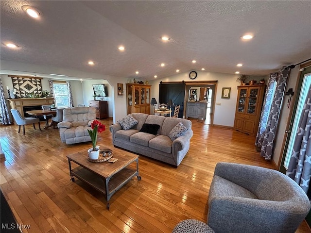 living room featuring lofted ceiling, light wood finished floors, a fireplace, and a textured ceiling