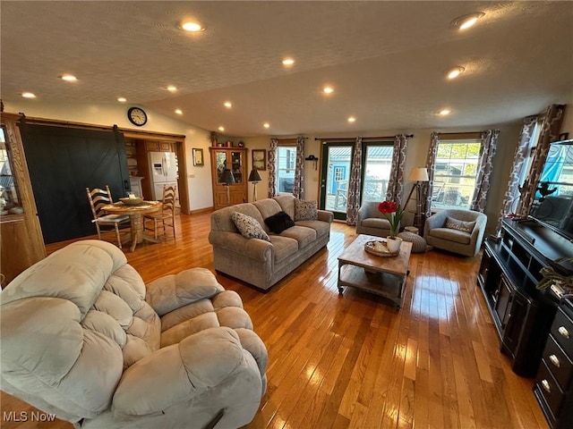 living room featuring lofted ceiling, a textured ceiling, a barn door, light wood-style flooring, and recessed lighting