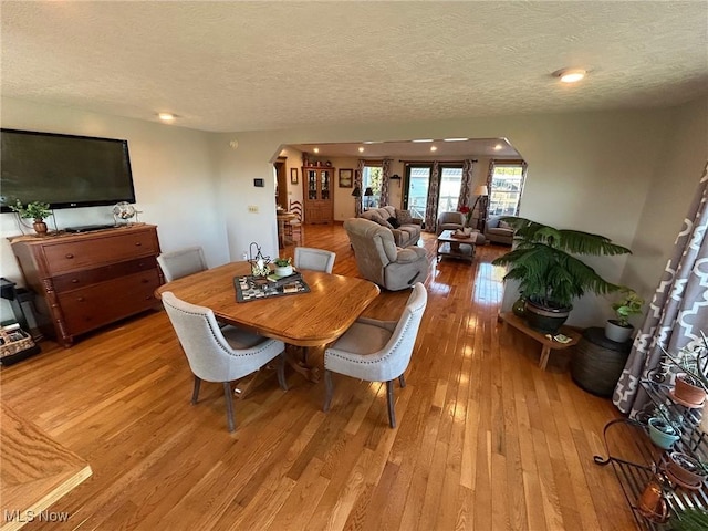 dining room featuring light wood-type flooring, arched walkways, and a textured ceiling