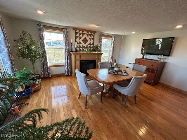 dining room with plenty of natural light, light wood-style flooring, a fireplace, and a textured ceiling