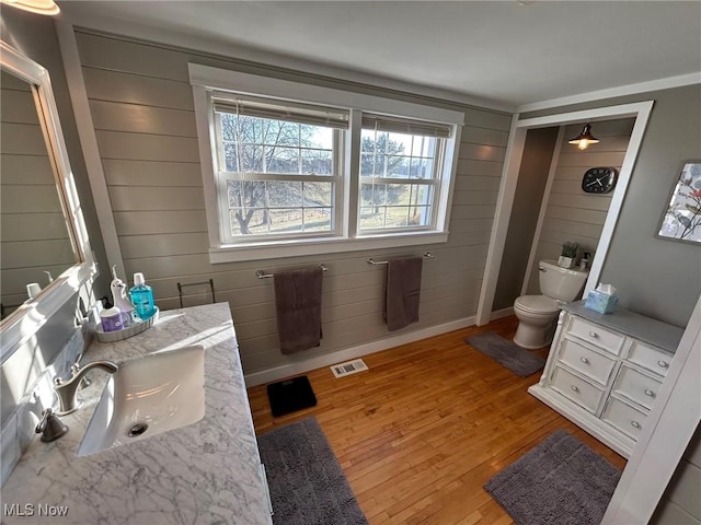 bathroom featuring visible vents, toilet, vanity, wood finished floors, and baseboards