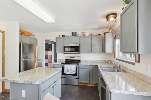 kitchen with appliances with stainless steel finishes, gray cabinets, a sink, and a center island