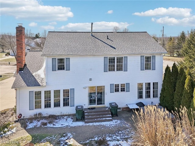 rear view of property with entry steps, roof with shingles, and a chimney