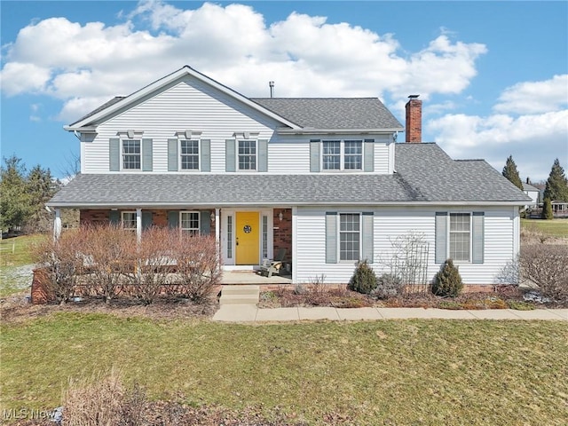 traditional-style house with covered porch, roof with shingles, a chimney, and a front yard