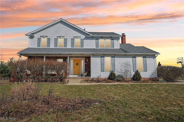 traditional-style home featuring covered porch, roof with shingles, a chimney, and a front yard