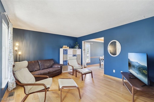 living area with light wood-type flooring, visible vents, and baseboards