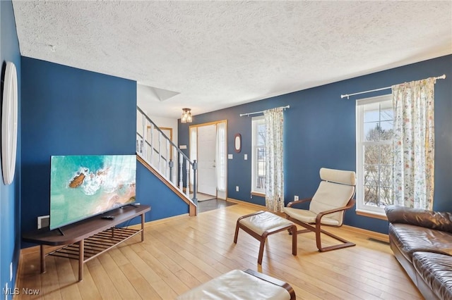 living area with wood-type flooring, a textured ceiling, baseboards, and stairs