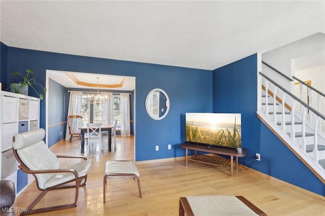 living area with a tray ceiling, stairs, baseboards, and wood finished floors