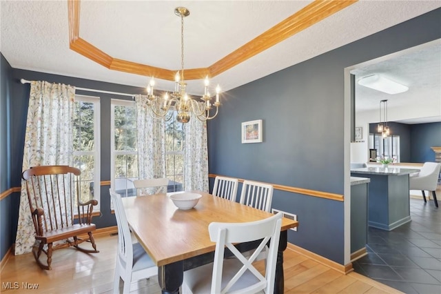 dining room with a tray ceiling, a healthy amount of sunlight, a notable chandelier, and baseboards