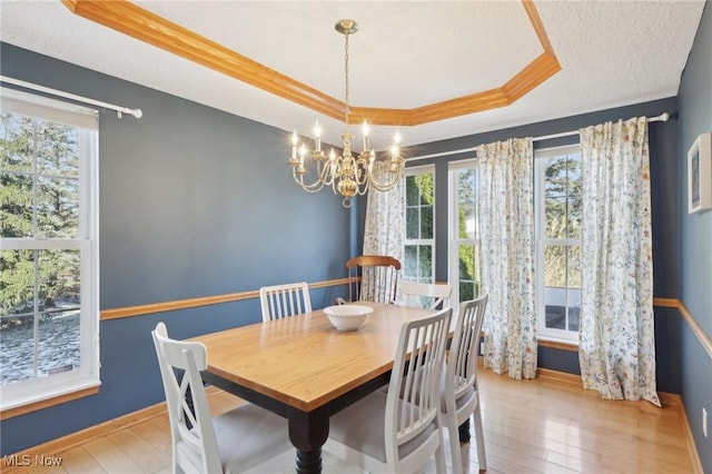 dining room with an inviting chandelier, wood-type flooring, baseboards, and a raised ceiling