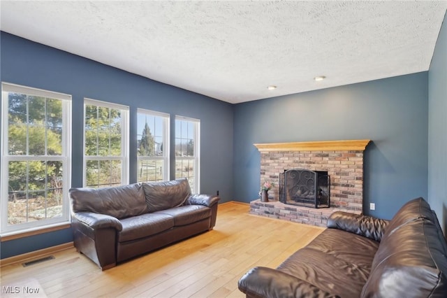 living room with a brick fireplace, visible vents, a textured ceiling, and hardwood / wood-style floors