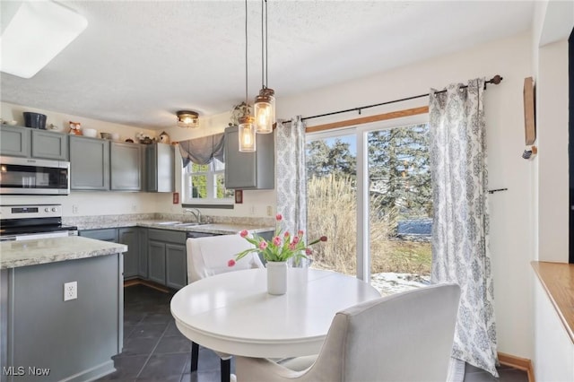 kitchen with stainless steel appliances, dark tile patterned flooring, a sink, hanging light fixtures, and gray cabinets