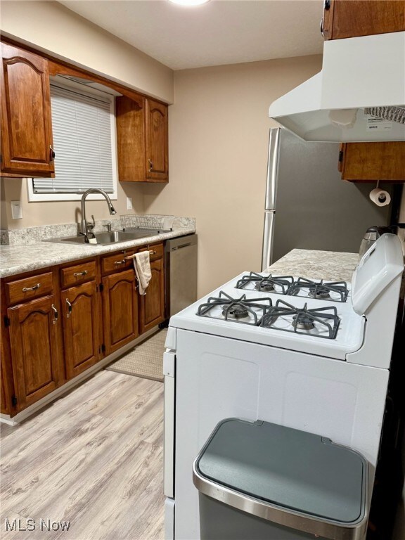 kitchen with under cabinet range hood, appliances with stainless steel finishes, brown cabinets, and a sink