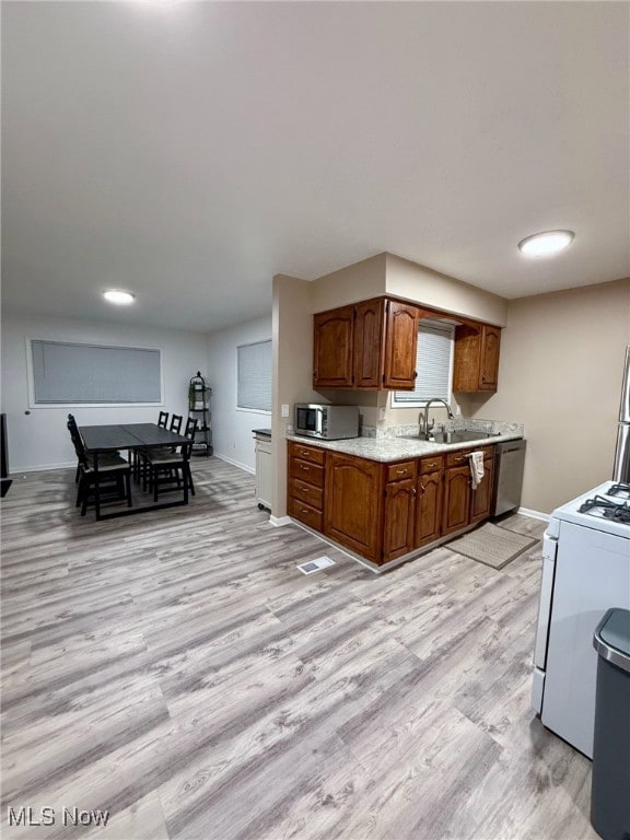 kitchen featuring stainless steel appliances, a sink, light wood-style floors, light countertops, and brown cabinetry