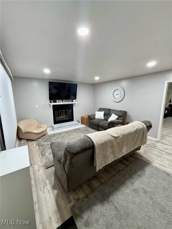 living area with recessed lighting, baseboards, wood finished floors, and a glass covered fireplace