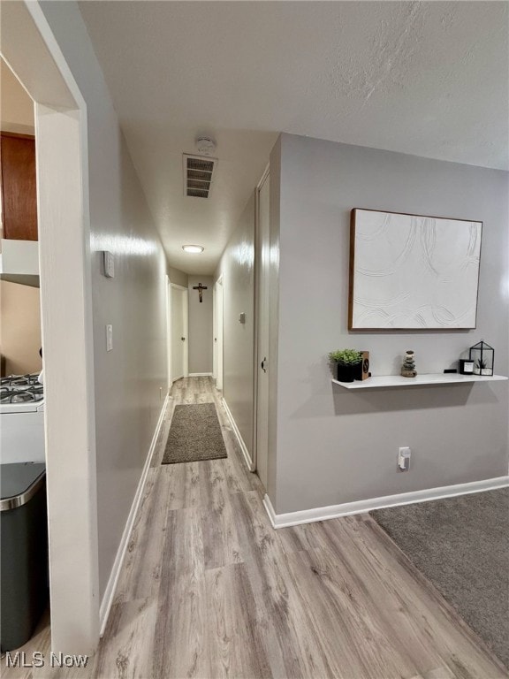 corridor featuring a textured ceiling, light wood-type flooring, visible vents, and baseboards