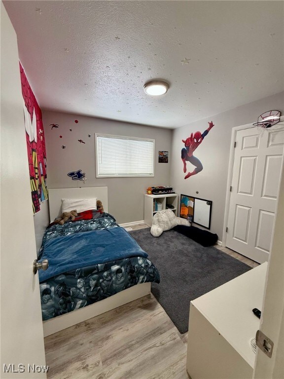 bedroom with a textured ceiling, baseboards, and wood finished floors