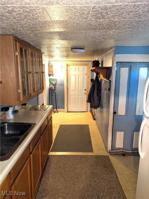 kitchen featuring light floors, glass insert cabinets, brown cabinetry, and a sink