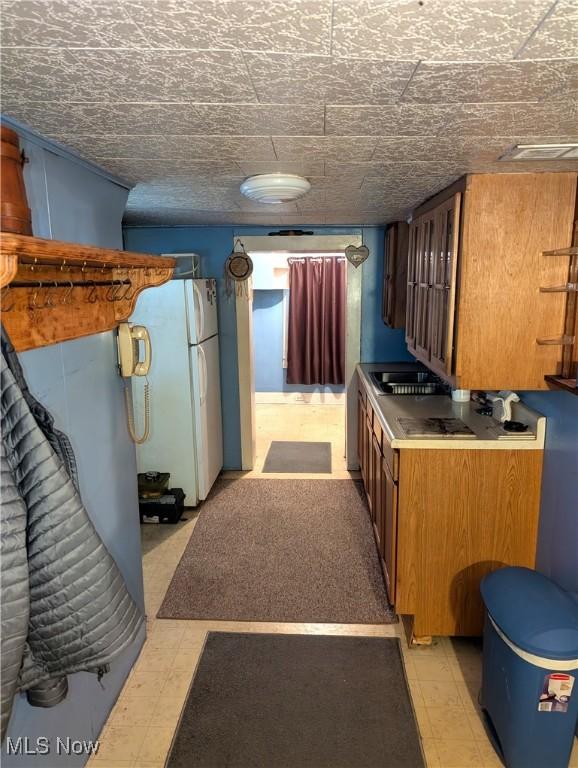 kitchen featuring light floors, a sink, freestanding refrigerator, and brown cabinets