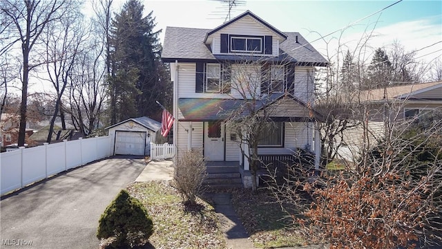 traditional style home with aphalt driveway, an outbuilding, fence, and a detached garage