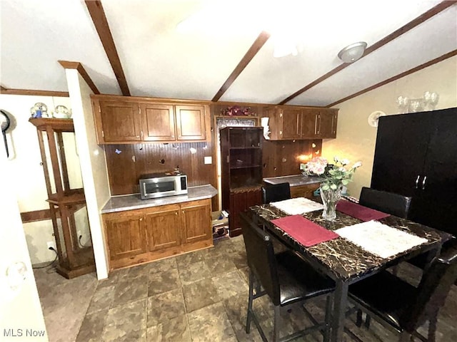 kitchen with vaulted ceiling with beams, stainless steel microwave, brown cabinetry, and light countertops