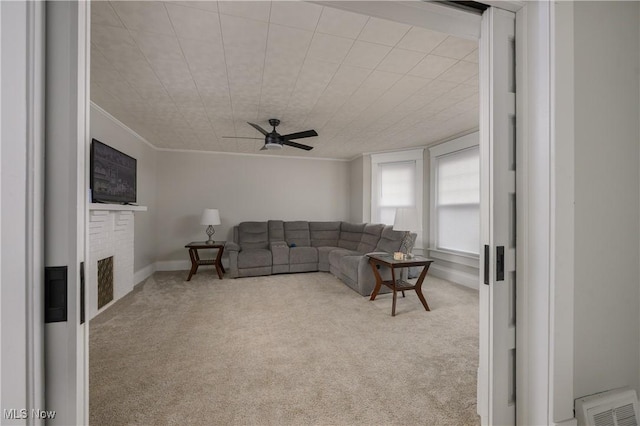 living room with carpet floors, ornamental molding, a fireplace, and a ceiling fan