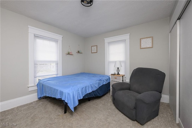 bedroom with a closet, light colored carpet, a textured ceiling, and baseboards