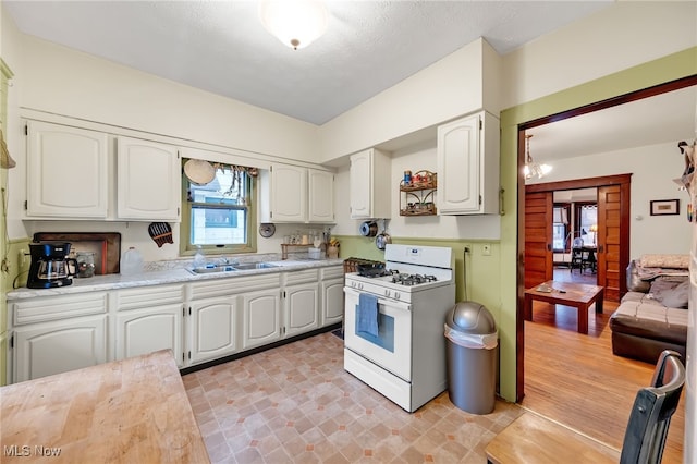 kitchen with white cabinets, white range with gas cooktop, light countertops, and a sink