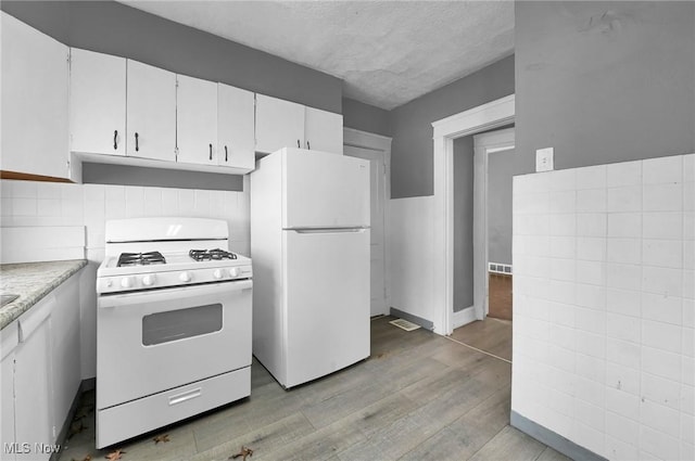 kitchen featuring white appliances, light wood-style flooring, under cabinet range hood, and white cabinetry