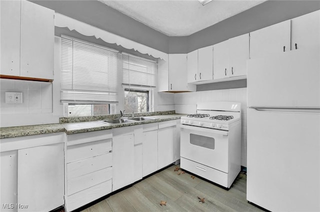 kitchen featuring light countertops, white cabinets, a sink, light wood-type flooring, and white appliances