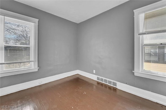 empty room featuring wood finished floors, visible vents, and baseboards