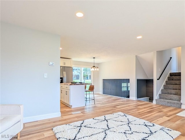 kitchen with light wood-style floors, a breakfast bar, white cabinets, and stainless steel refrigerator with ice dispenser