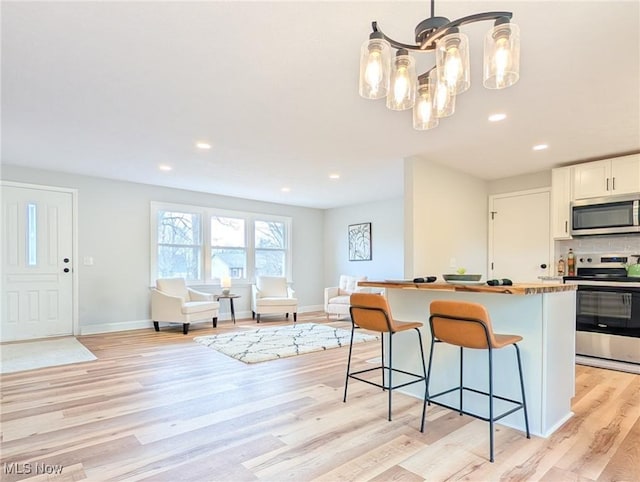 kitchen with appliances with stainless steel finishes, open floor plan, light wood-type flooring, a kitchen bar, and a chandelier