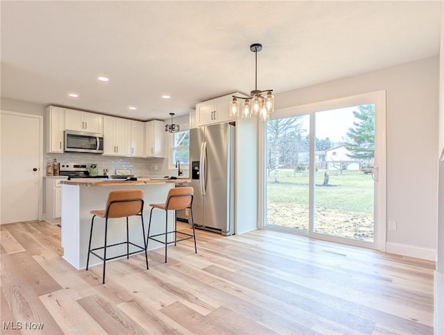 kitchen with white cabinets, a kitchen island, stainless steel appliances, light wood-type flooring, and backsplash