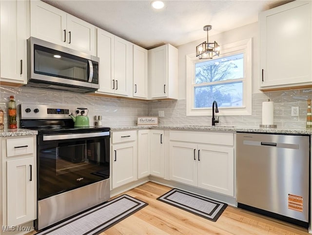 kitchen featuring stainless steel appliances, a sink, white cabinets, light wood-style floors, and tasteful backsplash