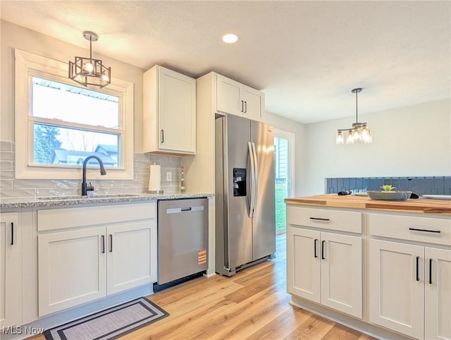 kitchen featuring light wood finished floors, stainless steel appliances, decorative backsplash, white cabinetry, and a sink