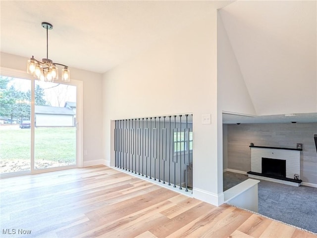 unfurnished living room with a fireplace, high vaulted ceiling, wood finished floors, a chandelier, and baseboards