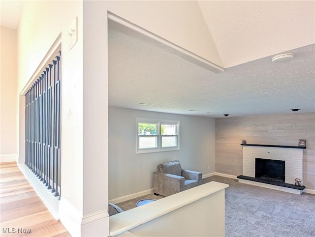 carpeted living area with a textured ceiling, a fireplace with raised hearth, and baseboards