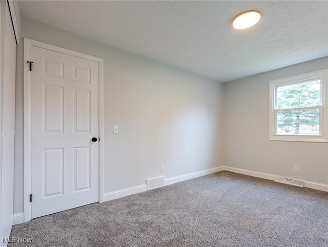 spare room featuring carpet floors, visible vents, a textured ceiling, and baseboards