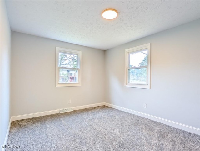 spare room featuring carpet floors, visible vents, a textured ceiling, and baseboards