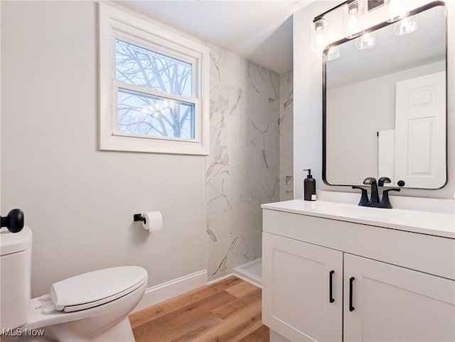 bathroom featuring toilet, wood finished floors, vanity, baseboards, and a marble finish shower