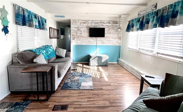 living area with a baseboard radiator, beam ceiling, visible vents, and wood finished floors