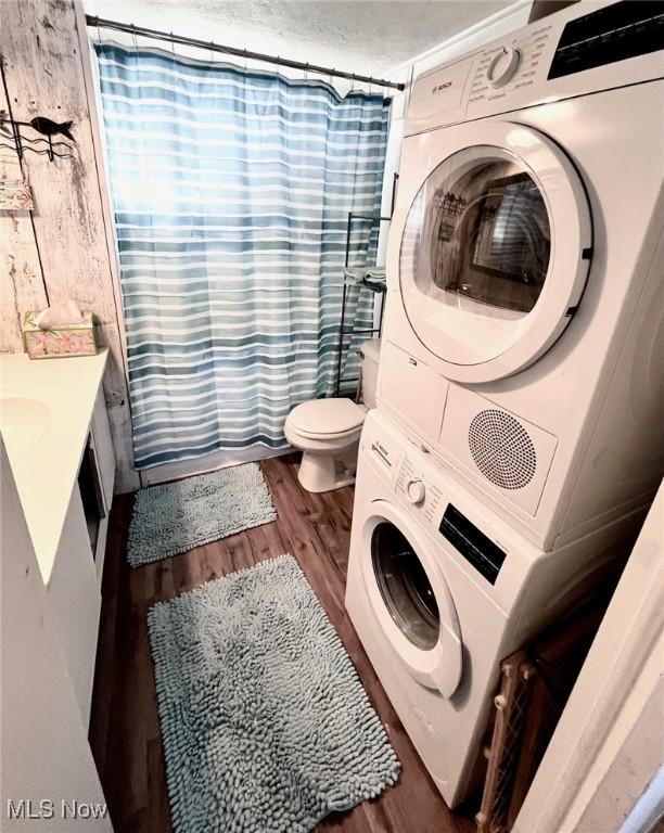 bathroom with a shower with shower curtain, toilet, wood finished floors, vanity, and stacked washing maching and dryer