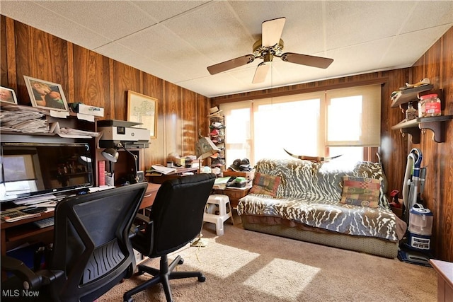 carpeted office with wooden walls and a ceiling fan