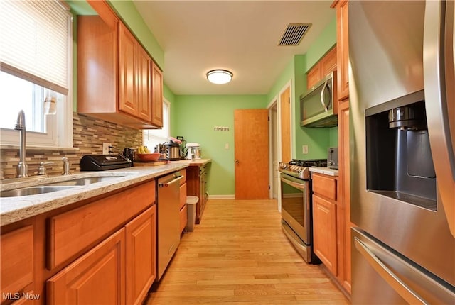 kitchen featuring visible vents, decorative backsplash, light wood-style flooring, stainless steel appliances, and a sink