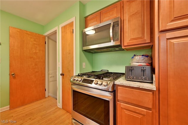 kitchen featuring light wood-type flooring, light stone countertops, baseboards, and stainless steel appliances