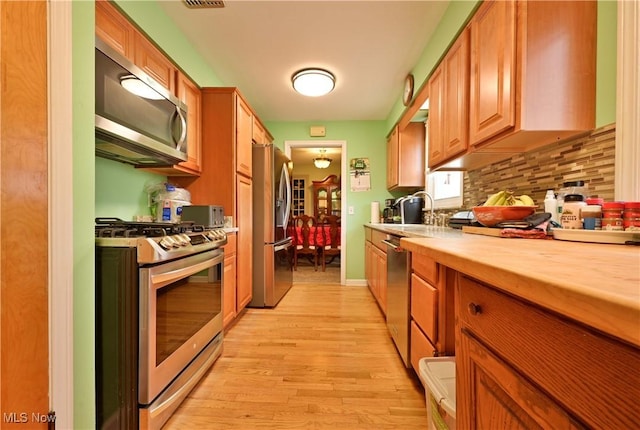 kitchen with tasteful backsplash, light wood-style flooring, appliances with stainless steel finishes, a sink, and baseboards