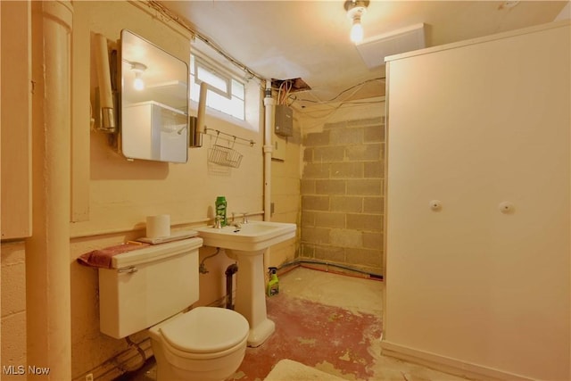 full bathroom with toilet, a sink, walk in shower, concrete block wall, and unfinished concrete floors