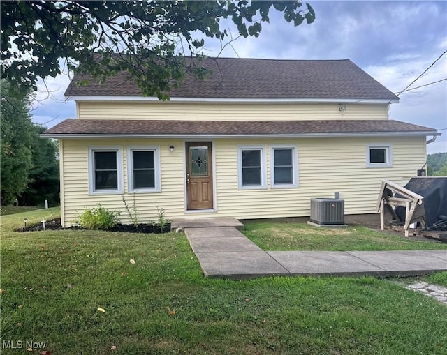 view of front of home with a shingled roof, a front yard, and central air condition unit